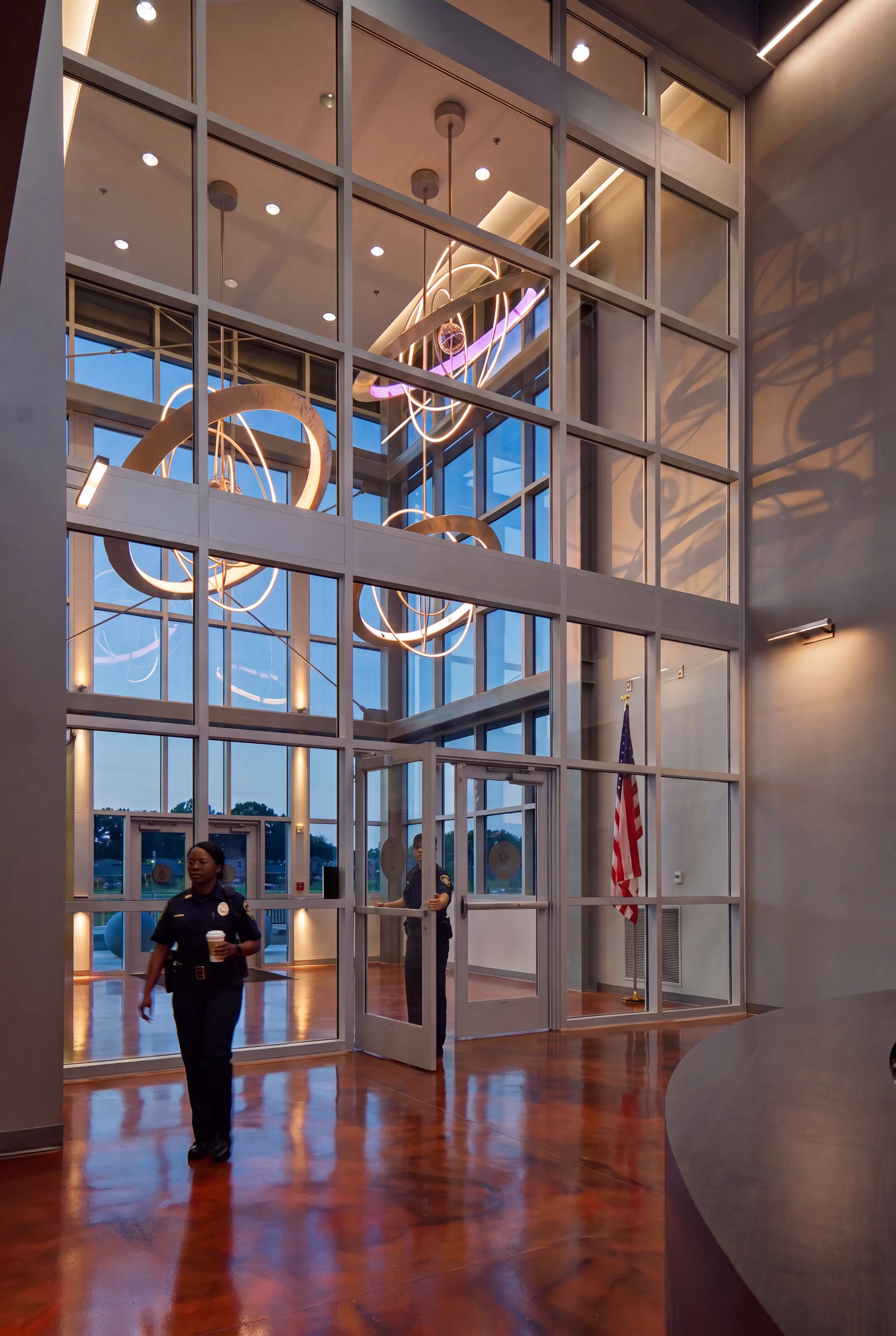 The two-story glass lobby at dusk, an officer crossing the floor