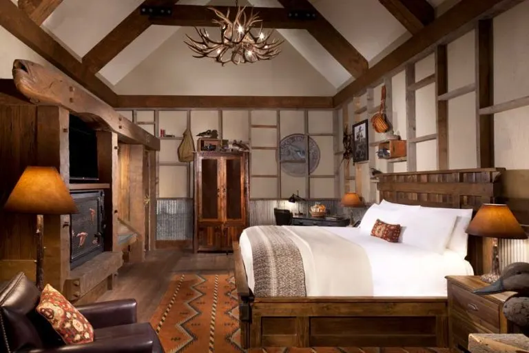 A duck-camp guest room with a timber ceiling, an antler chandelier and a log bed