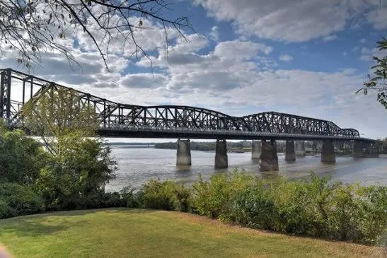 The bridge's steel truss spans from a grassy riverbank