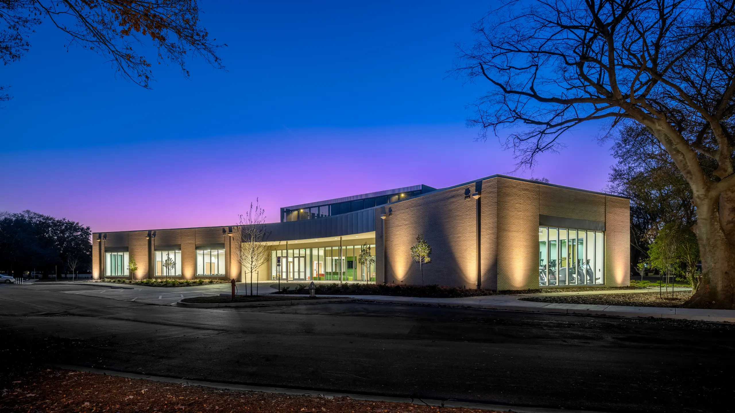 The community center at dusk, its glazed front lit under a purple sky