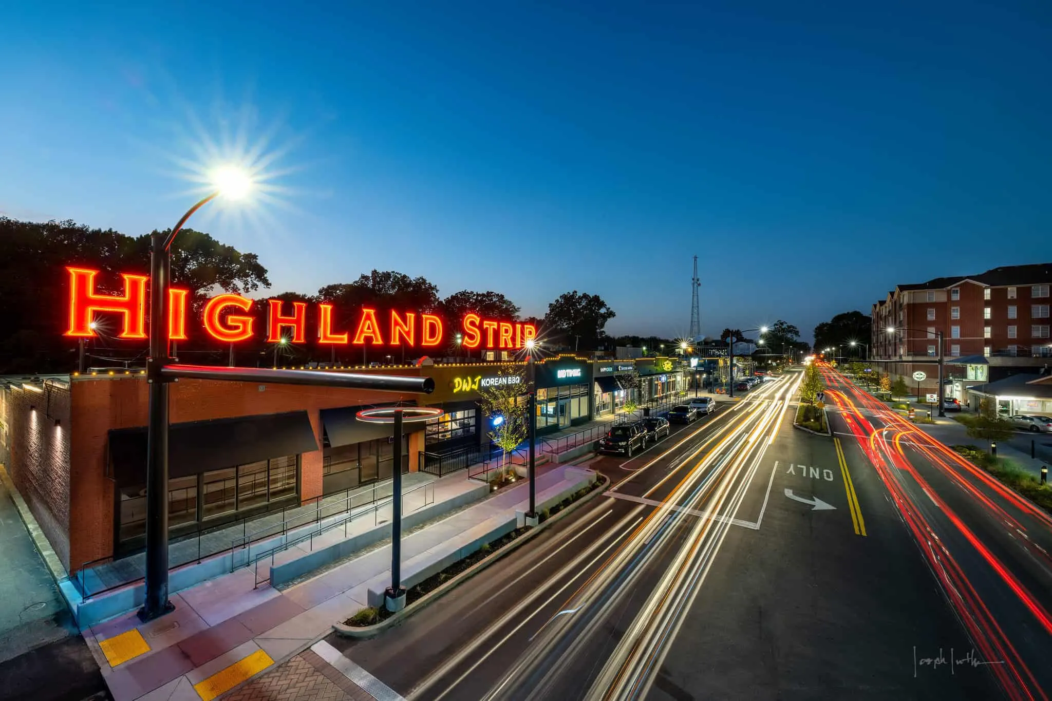 The Highland Strip sign in neon over traffic trails at dusk