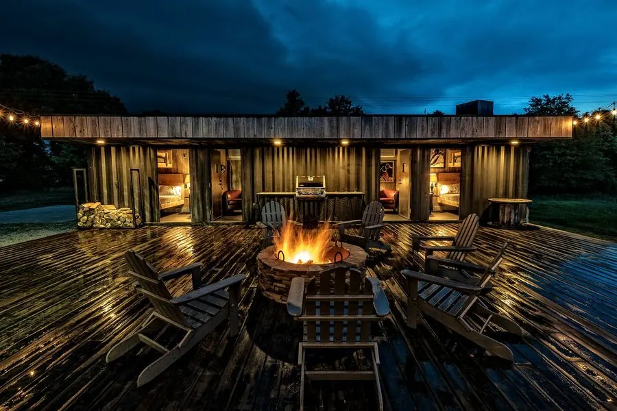 The lodge front at dusk, rooms open onto the rain-wet deck around a lit fire pit