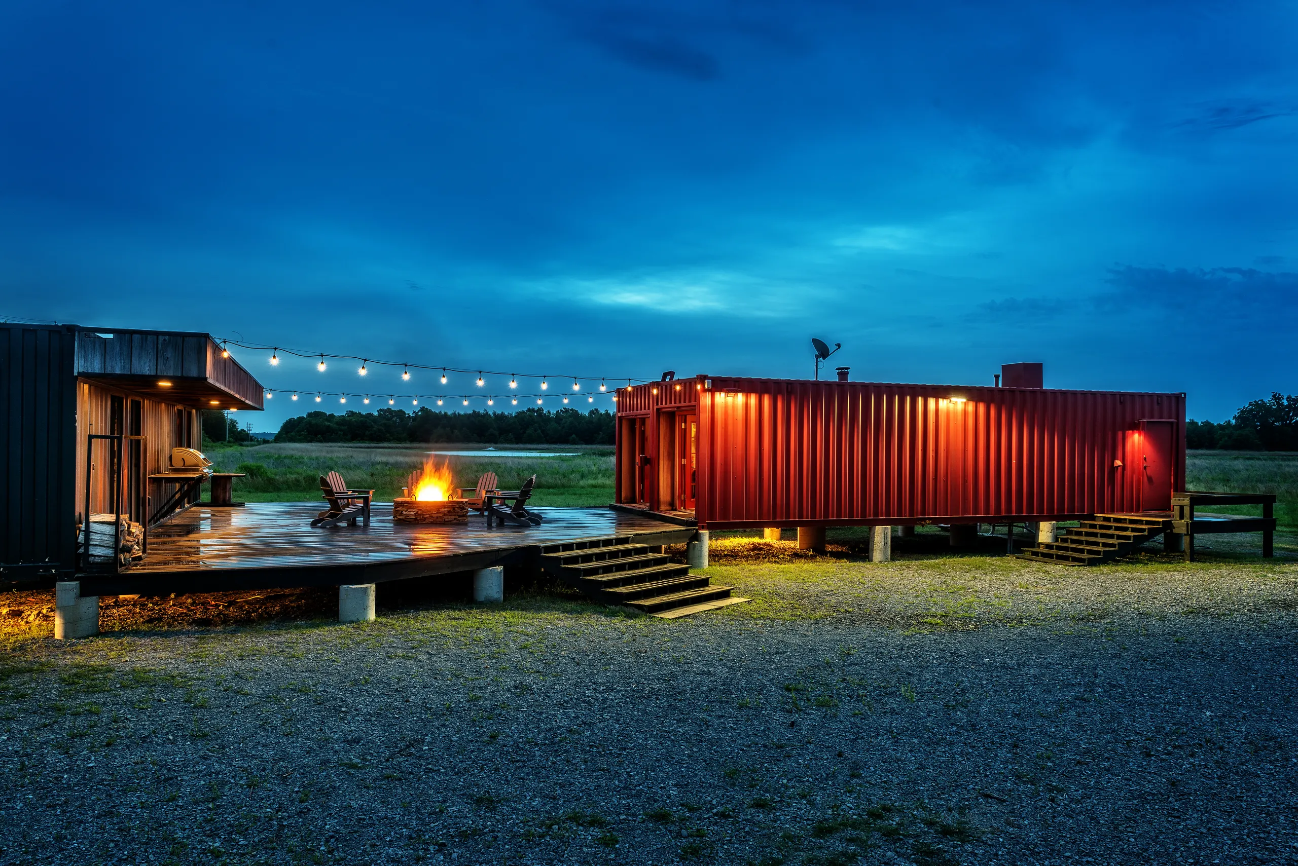 The lodge and deck across the field at nightfall, the fire pit lit