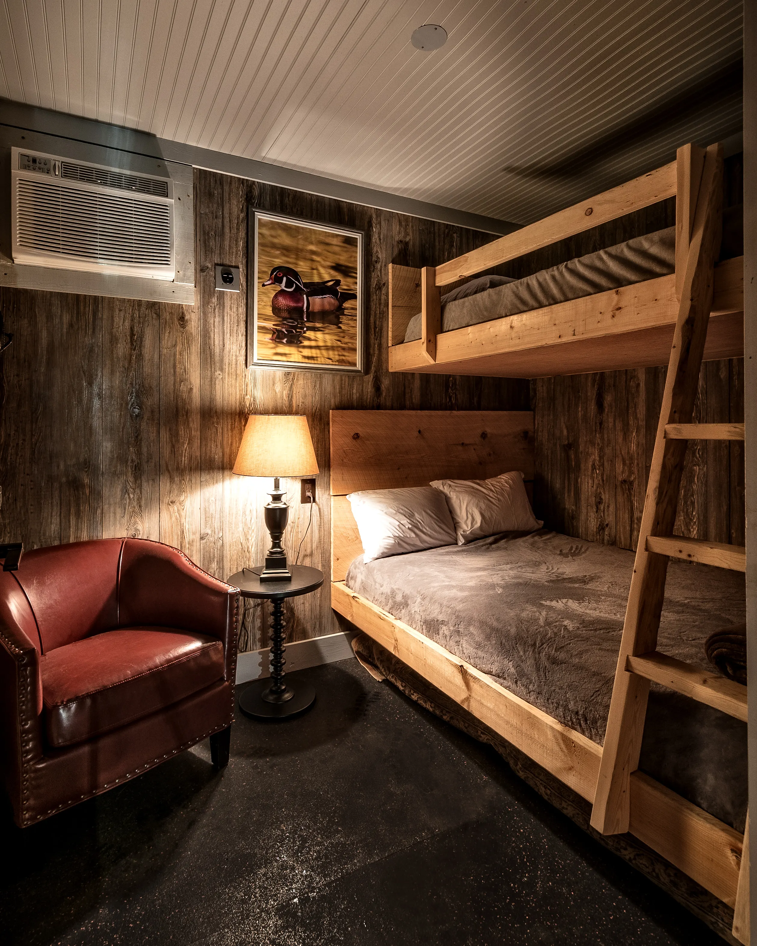 A bunk room with timber bunks, a red leather armchair and a bedside lamp