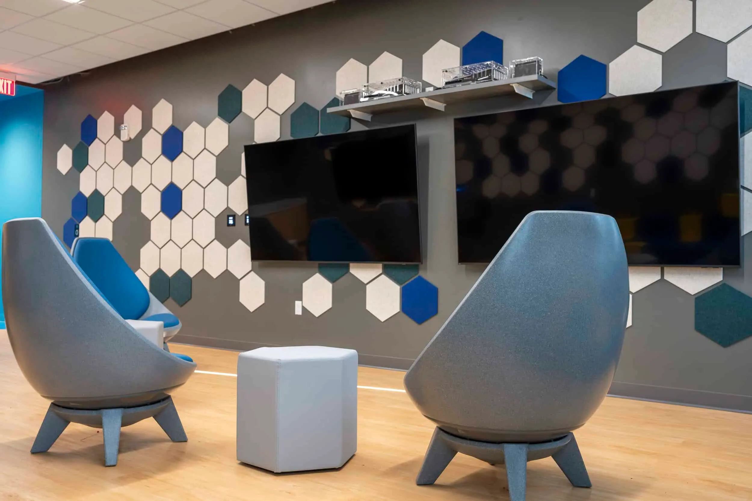 A lounge with gray chairs before a hexagon-tiled wall