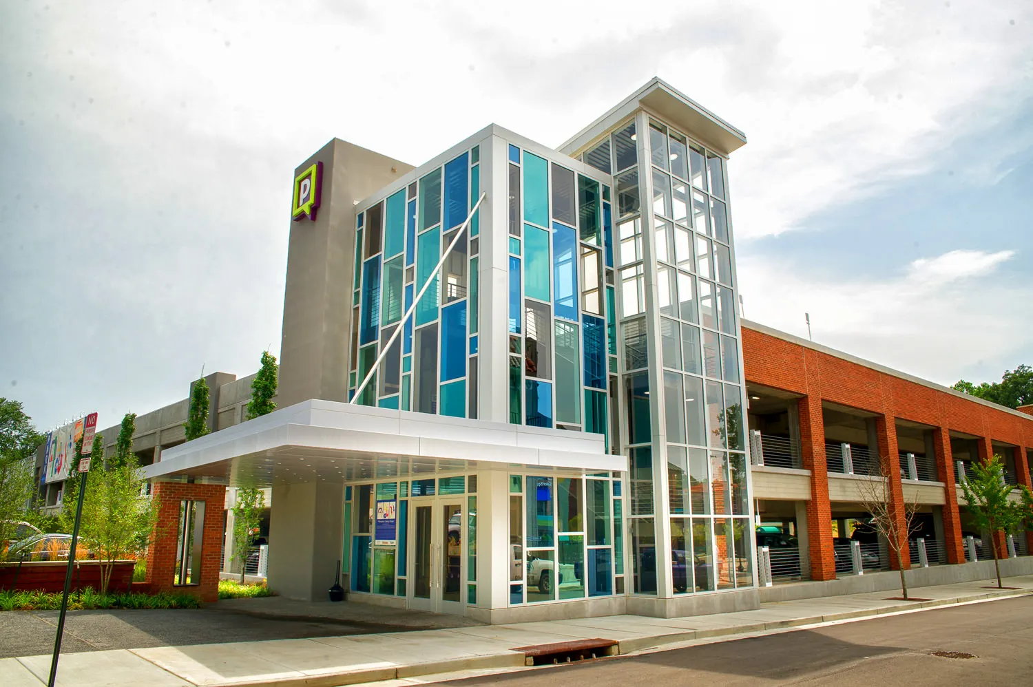 The glass stair tower and entry canopy on the street corner, the red brick garage beyond