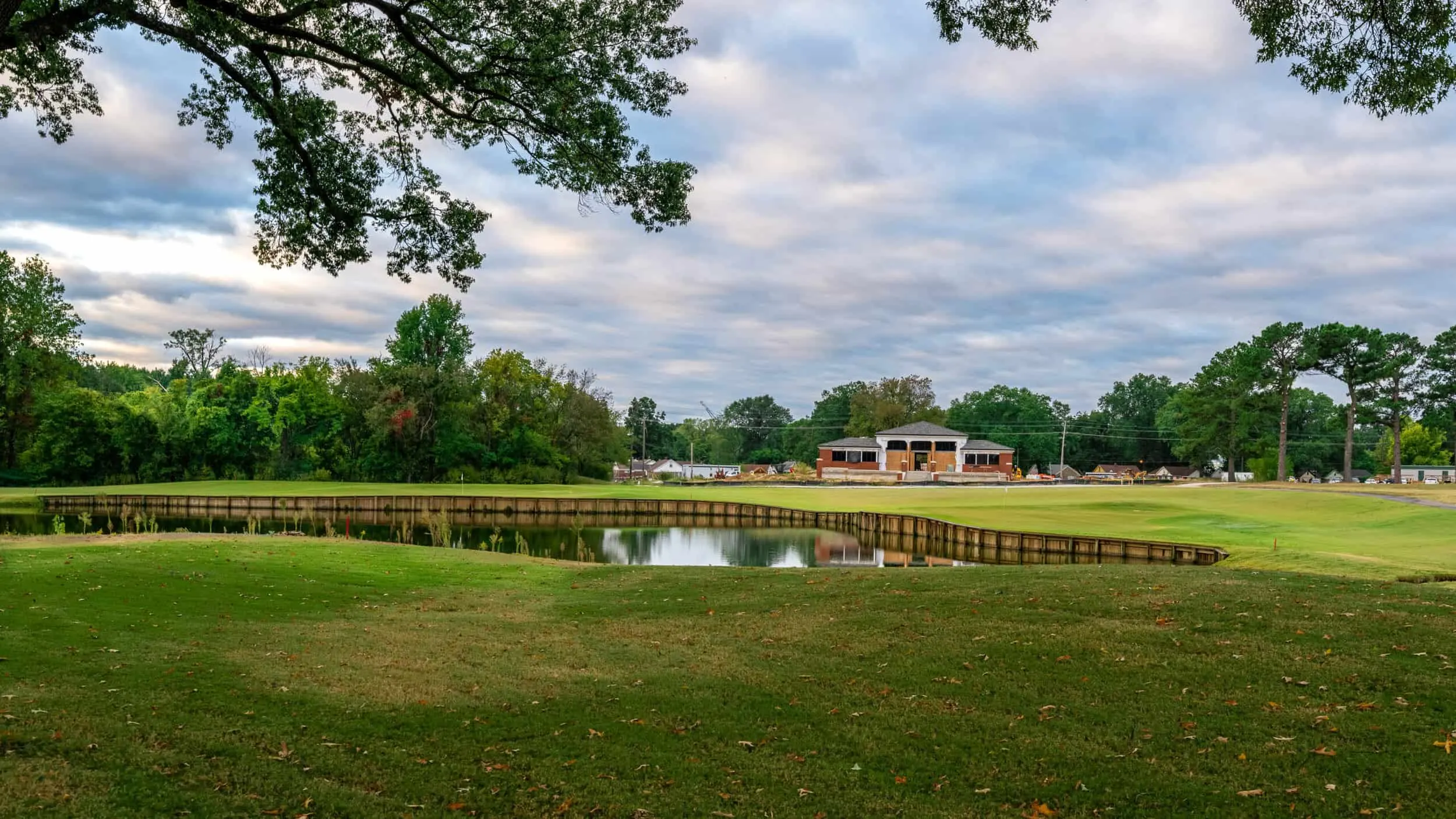 A pond and boardwalk with the clubhouse beyond, under a dramatic sky