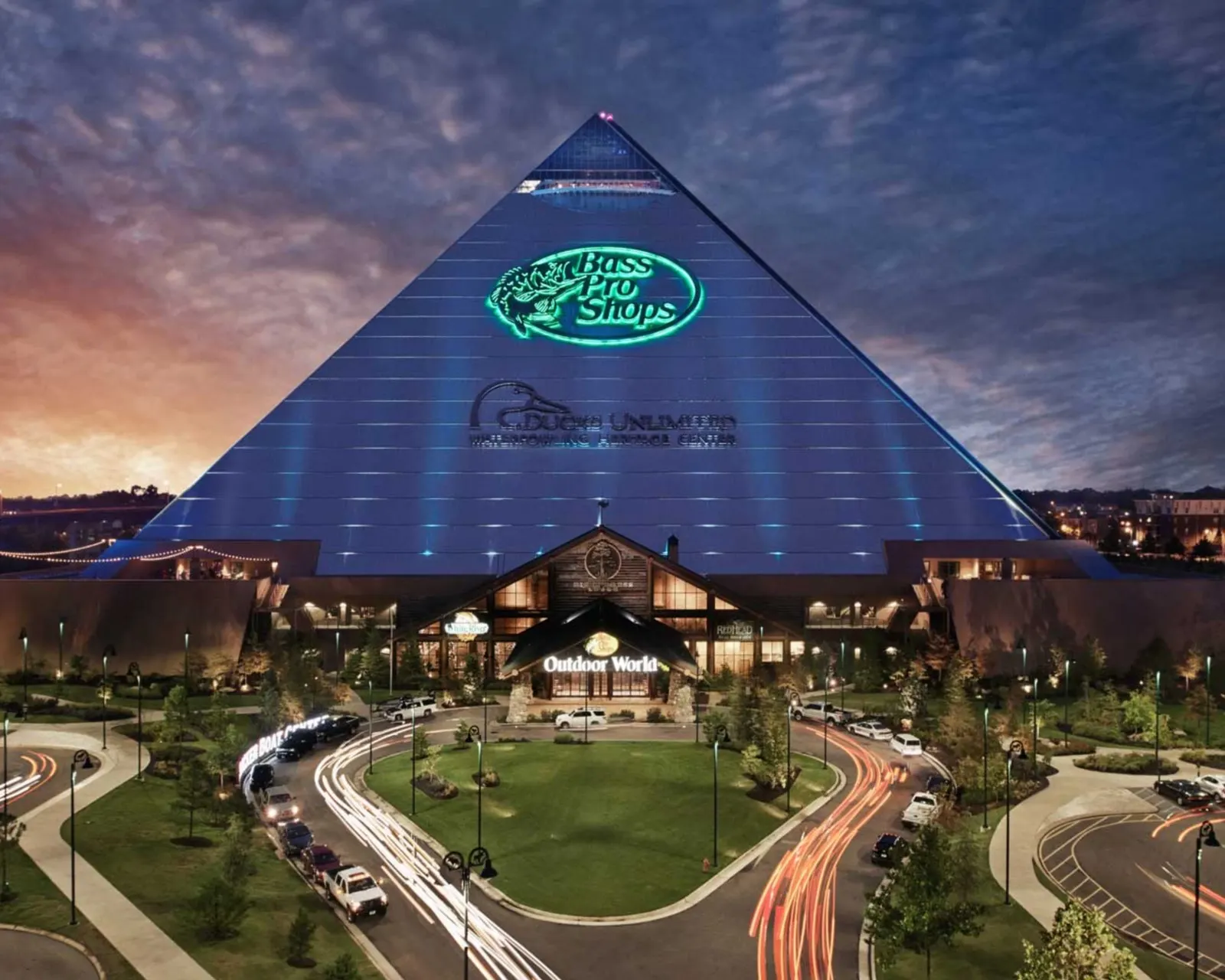 The Pyramid's timber entry lodge lit at dusk, headlight trails curving through the forecourt