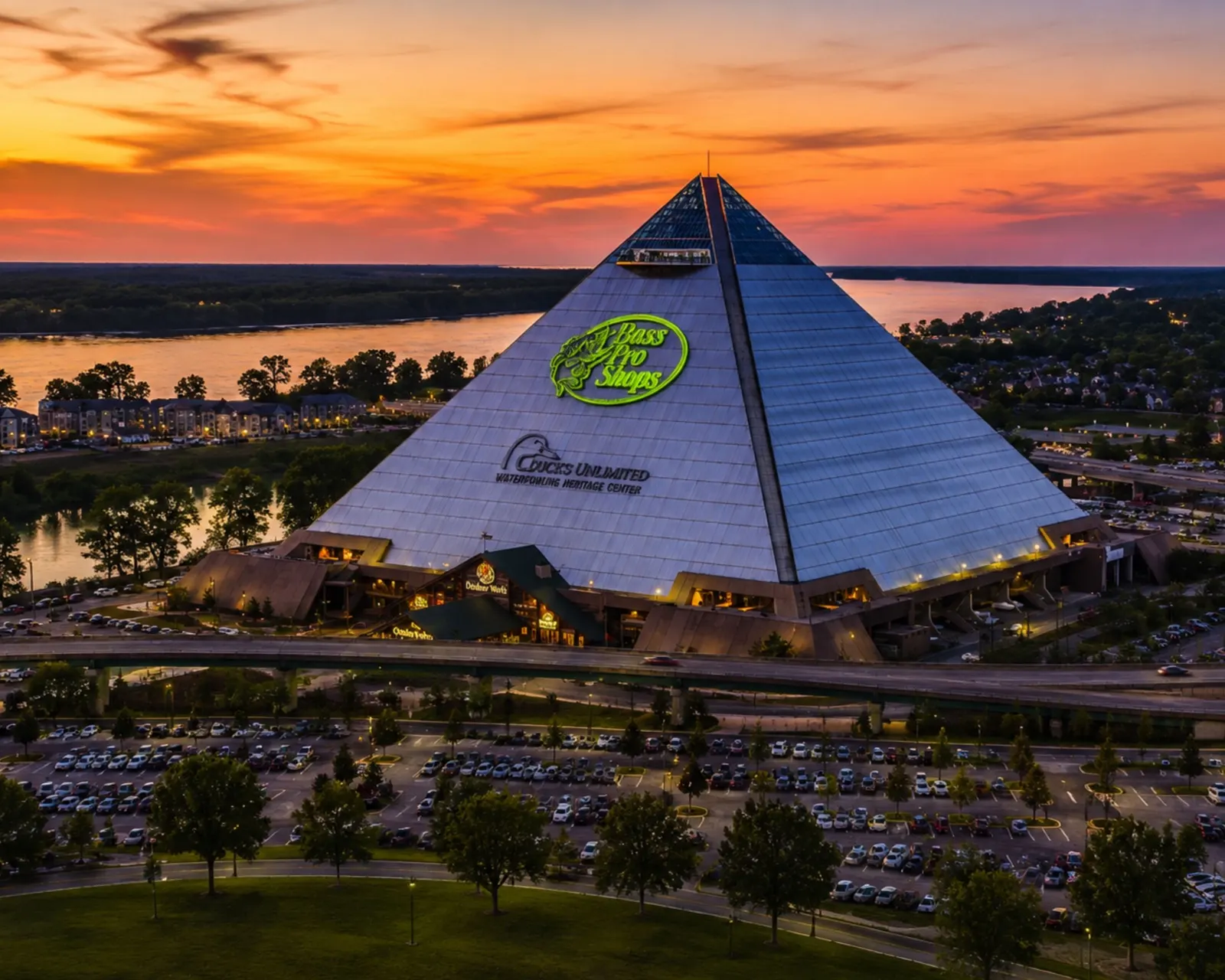The Pyramid from the air at sunset, its glass faces catching an orange sky above the Mississippi River