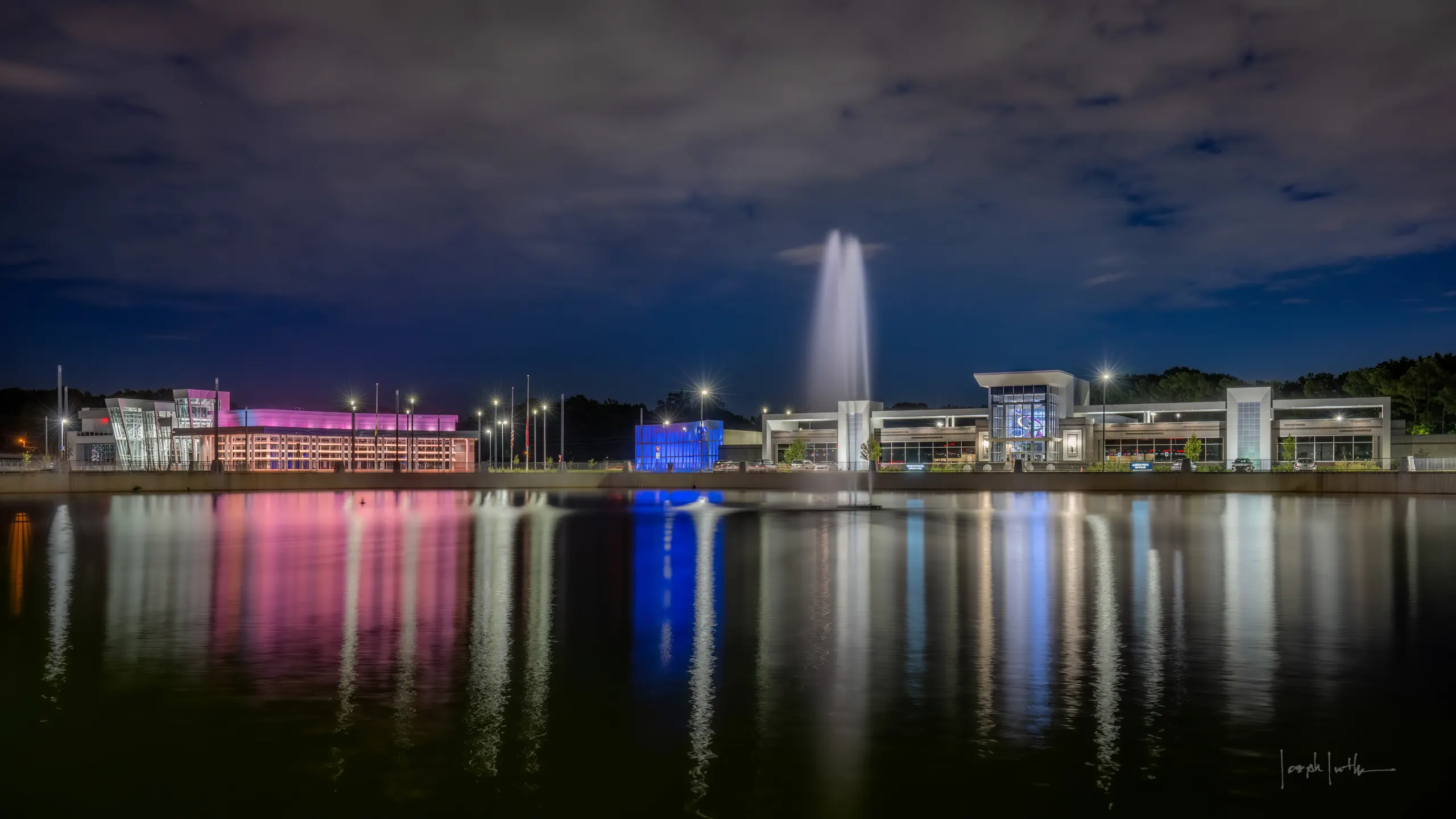 Raleigh Springs Civic Center at night, the town center lit across the lake with the fountain at its middle